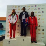 Elinah Philip proudly bears the BVI flag as she collects her gold for her first place finish in a time of 28.71 in the Girls 13-14 50m fly. She is flanked by silver medalist, Keely Maduro, of Aruba, and Amira Pilgrim of Trinidad and Tobago.